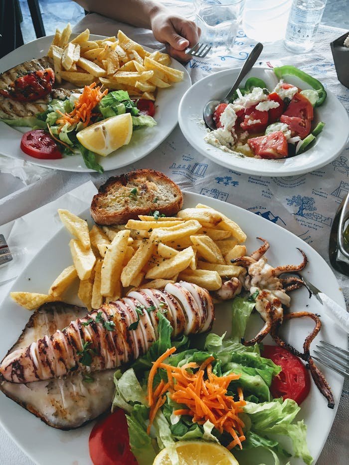 hero-img-02 A vibrant Greek meal featuring grilled squid, fresh salad, and fries, perfect for a seafood lover.
